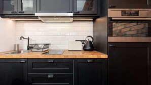 Una cocina moderna con armarios oscuros, salpicadero de azulejos blancos, un lavamanos de acero inoxidable y un horno empotrado.