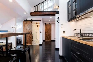 Une cuisine moderne avec des meubles de couleur sombre, une table à manger en bois et une chambre à coucher située en mezzanine, offrant une vue dégagée.