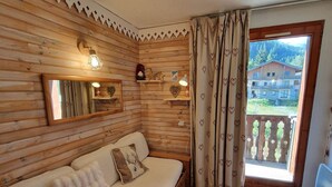 A cozy wooden cabin room with a sofa, a mirror, and a window with curtains. - Charming studio for 2-3 people, 17m² south-facing in Valfréjus (Valfréjus)