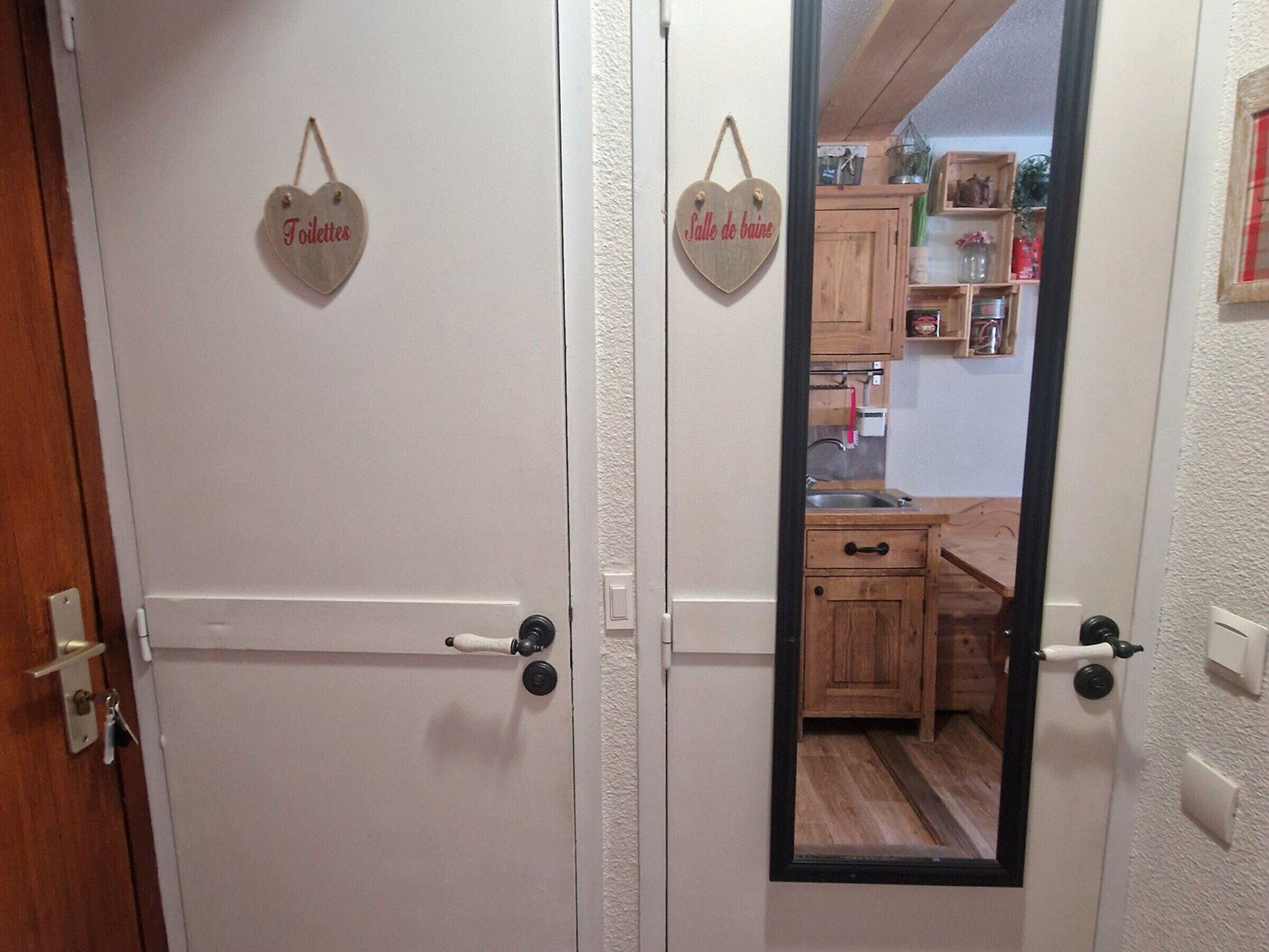 Une pièce avec deux portes blanches, chacune ornée d’une enseigne en forme de cœur au-dessus de la poignée. L’une des enseignes indique « Toilettes » et l’autre indique « Salle de bain ».