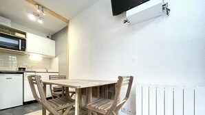 A modern kitchen with white cabinets, a built-in microwave, and a dining area with a wooden table and chairs. - Charming Studio for 4 in Resort Center, Steps from Slopes (Valfréjus)