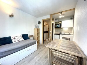 A compact living space with a bed, a wooden table, and a kitchenette.