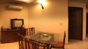 A dining area with a glass-top table, wooden chairs, a dark wooden cabinet, and a wall-mounted air conditioner. - The place to stay when you are in New Delhi (New Delhi)