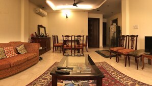 A living room with a sofa, a coffee table, a dining table with chairs, a ceiling fan, and a refrigerator. - The place to stay when you are in New Delhi (New Delhi)