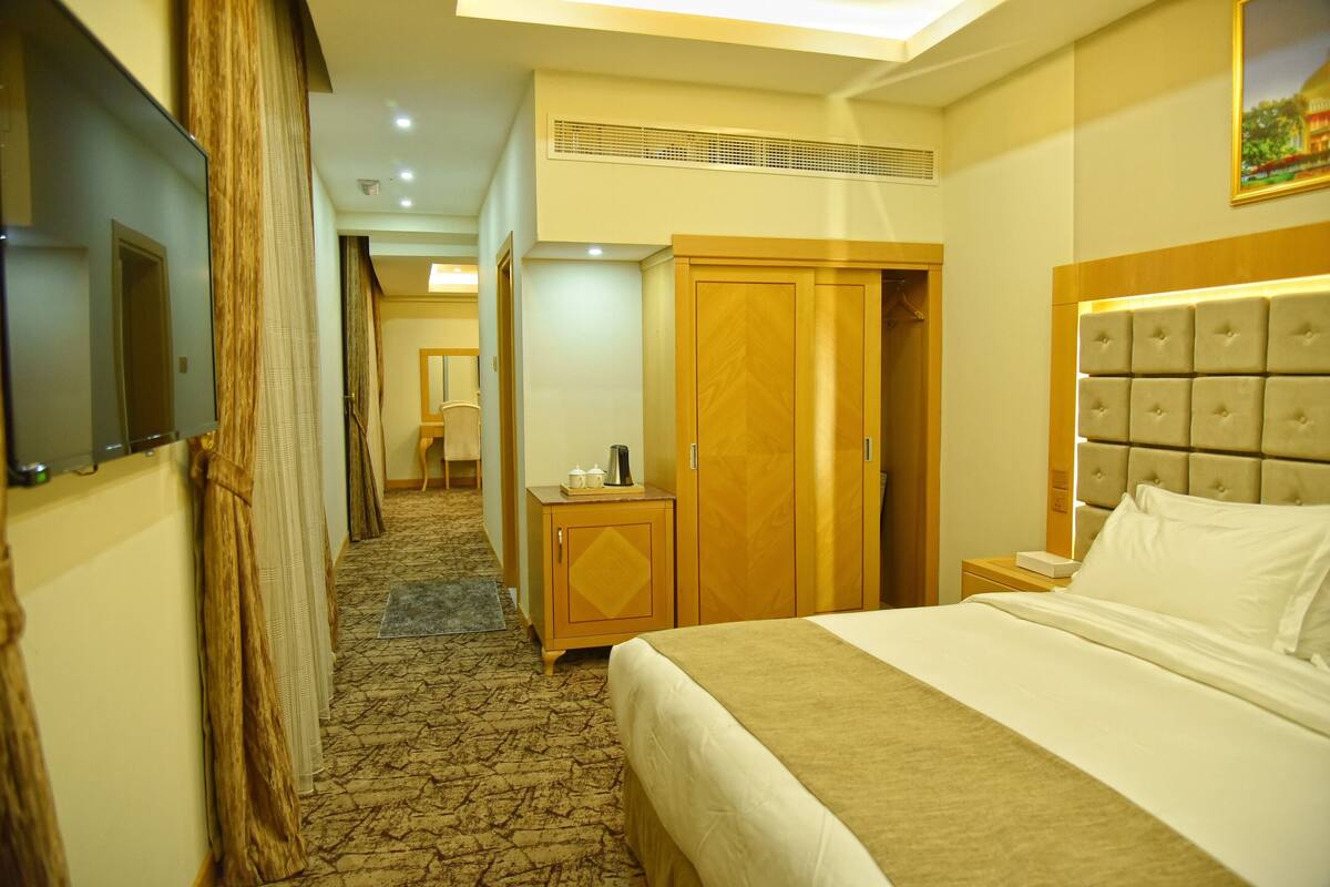 Une chambre d’hôtel avec un lit, une armoire, une table de chevet, une télévision et une porte.