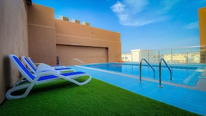 Una piscina en la azotea con agua azul, rodeada por un muro bajo y una barandilla de vidrio.