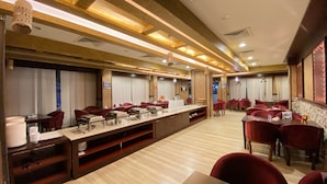 Un restaurante espacioso con una barra larga, sillas rojas y techo de madera.