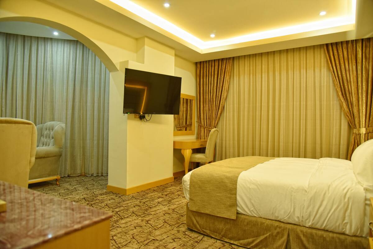 Une chambre d’hôtel comprenant un lit, un bureau, une chaise, un téléviseur fixé au mur et une grande fenêtre avec des rideaux.