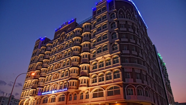 Un hotel de varios pisos con detalles arquitectónicos ornamentales, incluyendo ventanas arqueadas y balcones, y señalización iluminada.