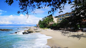 A beach with waves, a thatched hut, and buildings with balconies. - 2 BR romantic Penthouse in Conchas Chinas with amazing views & beach access (Puerto Vallarta)