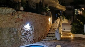 A nighttime pool area with stone walls, a staircase, and lounge chairs. - 2 BR romantic Penthouse in Conchas Chinas with amazing views & beach access (Puerto Vallarta)