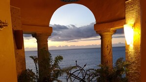 A view through an archway with columns, potted plants, and a decorative metal piece, overlooking a body of water at sunset. - 2 BR romantic Penthouse in Conchas Chinas with amazing views & beach access (Puerto Vallarta)