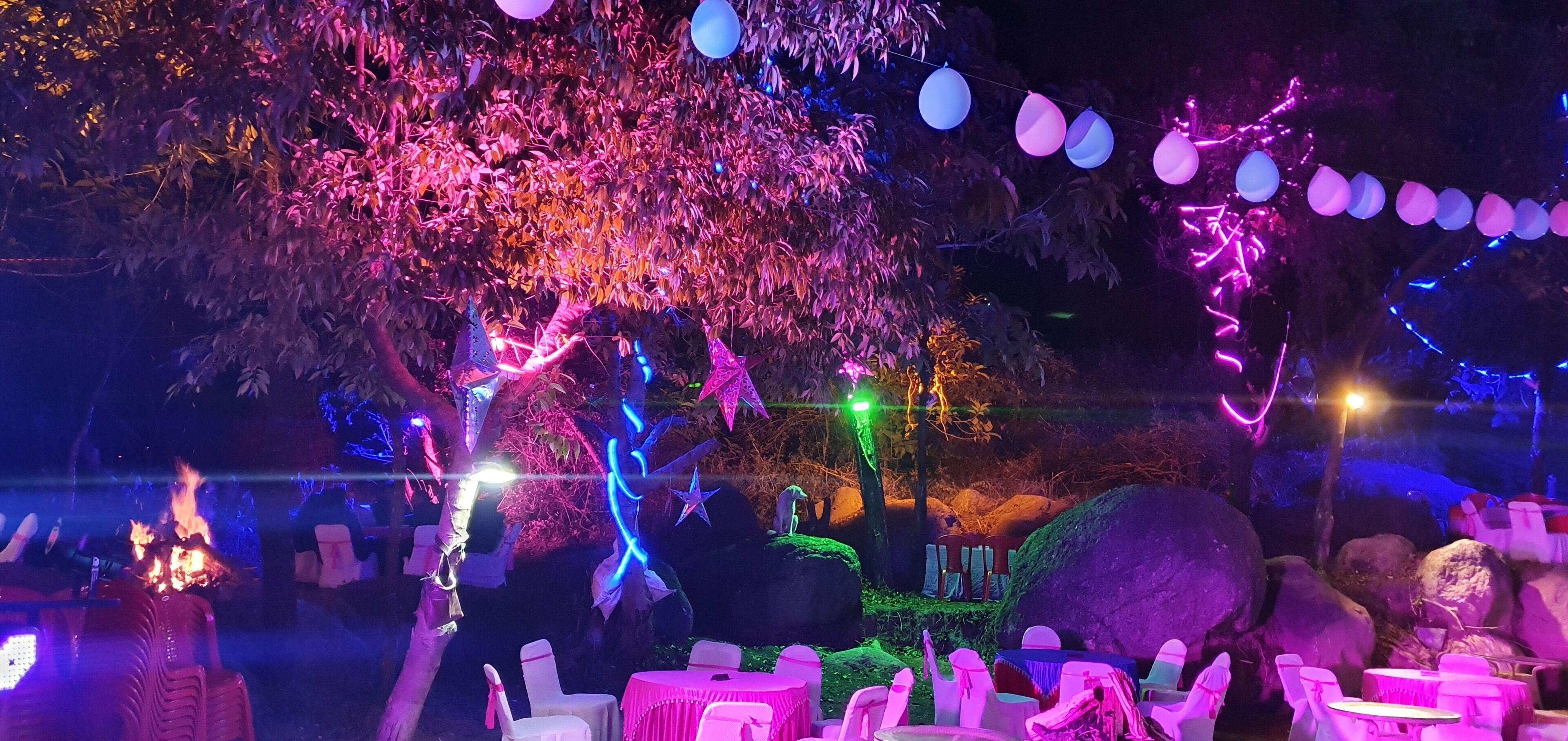 Un área de estar al aire libre con mesas y sillas, decorada con luces de hilo y globos.