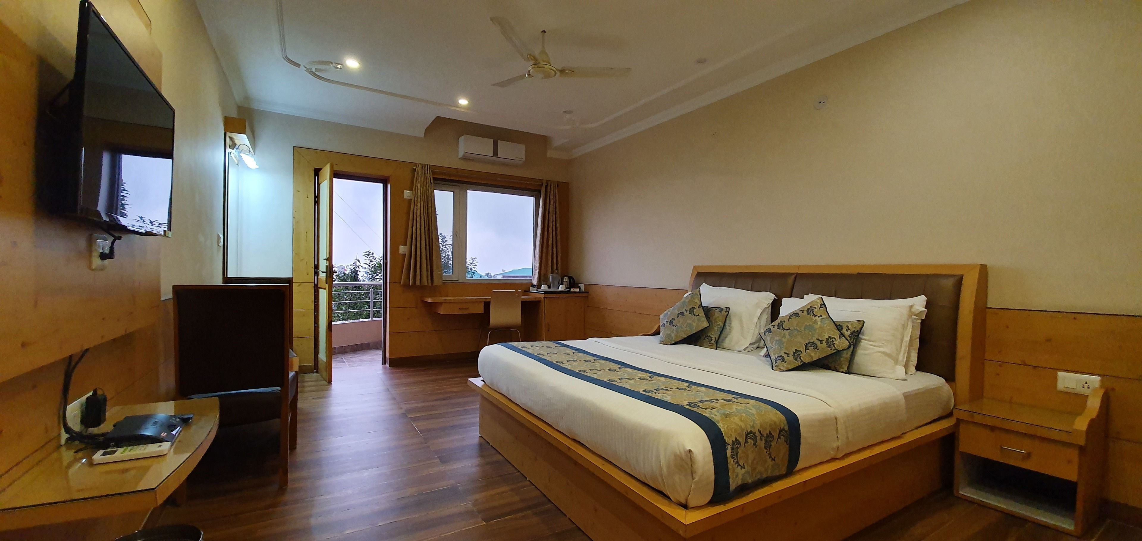 A bedroom with a bed, bedside tables, a desk, a television, and a ceiling fan.