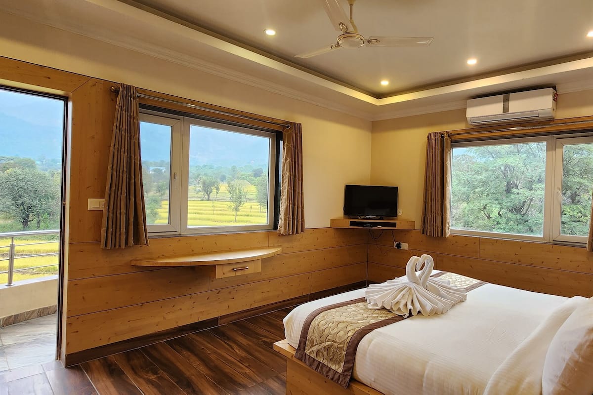 A bedroom with wooden paneling, a bed with white linens, a flat-screen TV, and large windows with curtains.