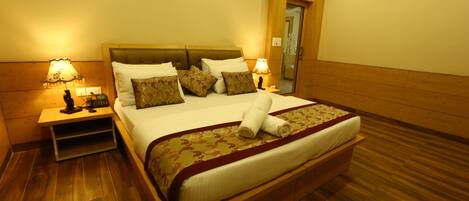 A neatly made bed with a wooden headboard, two bedside tables with lamps, and a wooden floor.