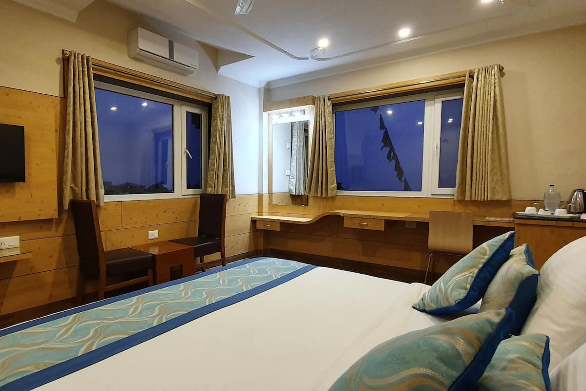 A hotel room with a bed, a desk, a chair, a television, and windows with curtains.