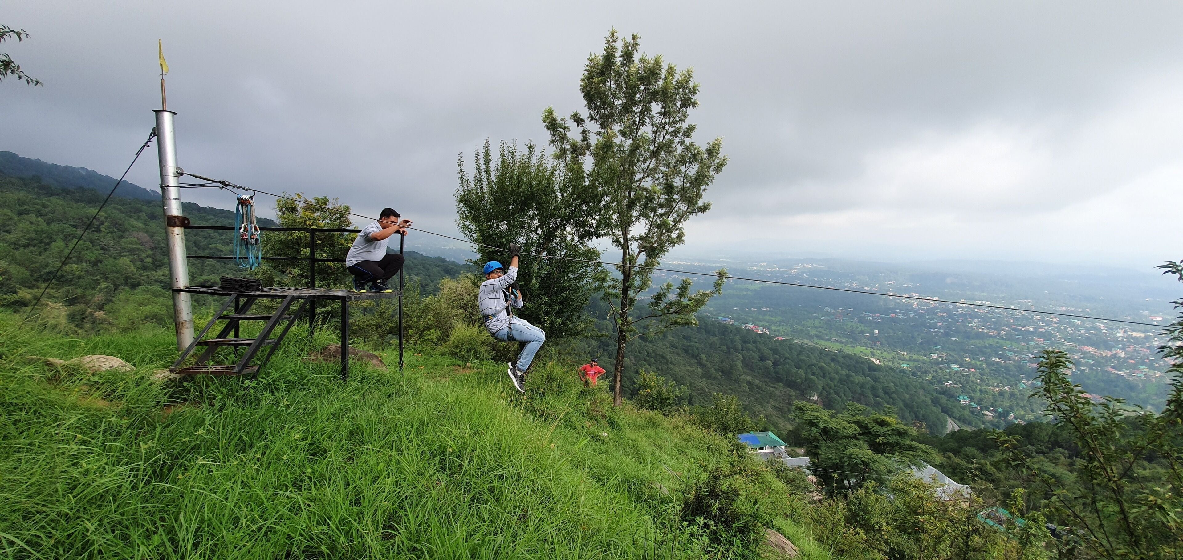 Una persona descendiendo por un cable en una ladera cubierta de hierba, con vistas a un valle.