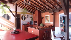 A kitchen with a red table, white chairs, and a brick oven. - Aloha Hostel Cabo Frio (Cabo Frio)