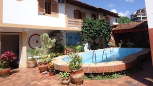 A courtyard with a swimming pool, potted plants, and a building with a tiled roof and windows. - Aloha Hostel Cabo Frio (Cabo Frio)