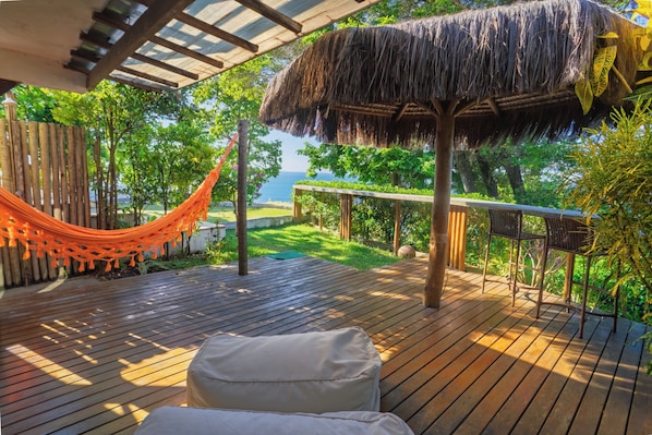 A wooden deck with a hammock, a thatched-roof structure, and a view of the sea. - Villa Giulia Morro (Cairu)