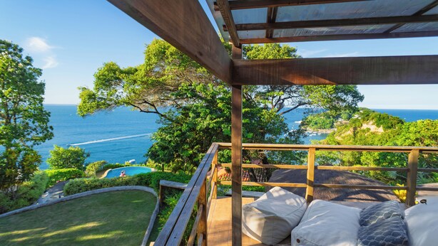 A wooden deck with a view of the sea, a pool, and lush greenery. - Villa Giulia Morro (Cairu)