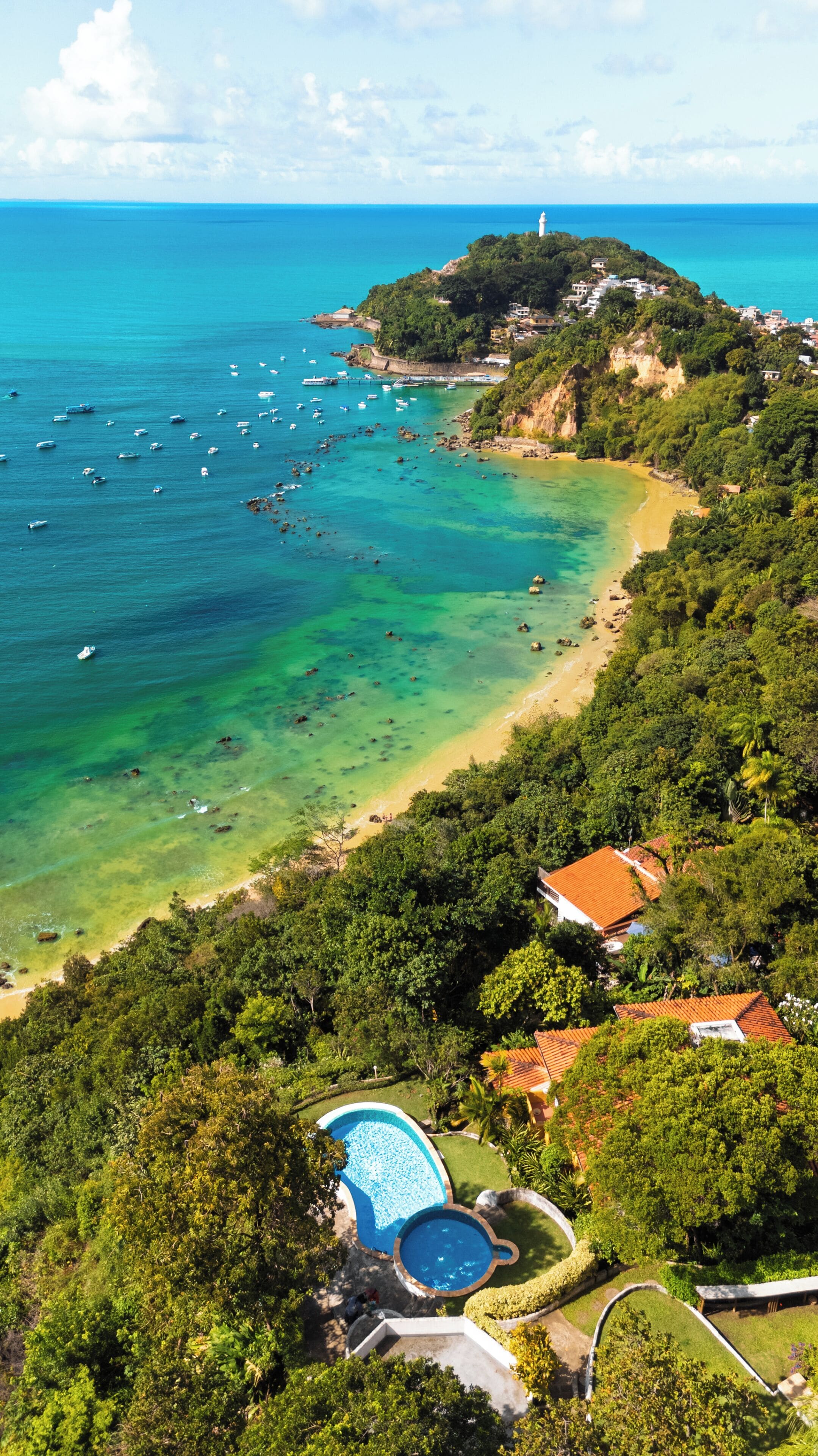 A coastal property with a swimming pool, beach access, and a lighthouse in the distance.