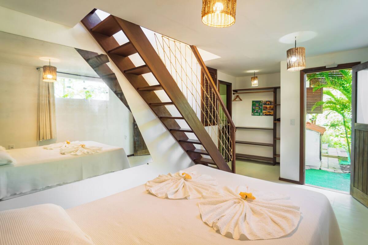 Une chambre d’hôtel avec un escalier en bois, deux lits et un balcon donnant sur un paysage verdoyant.