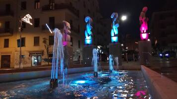 Una fuente iluminada con esculturas en un entorno urbano nocturno.