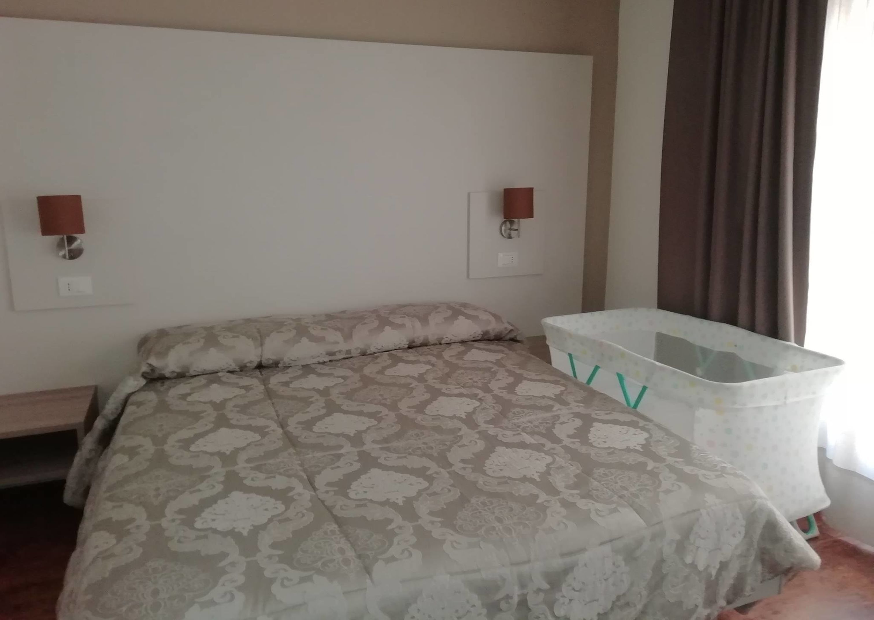 Un dormitorio con una colcha estampada, una mesita de noche, una lámpara de pared y un contenedor de plástico.