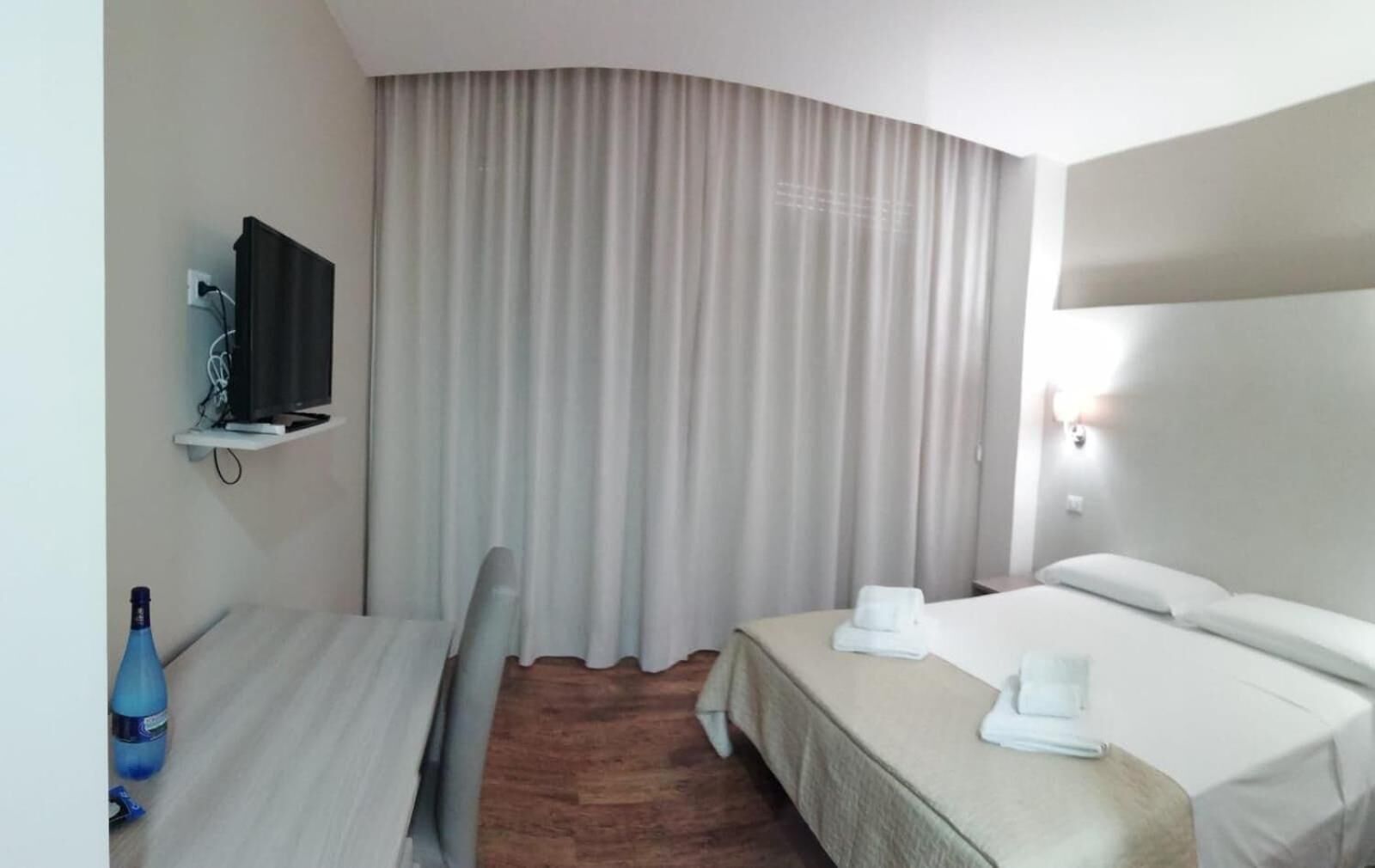 Una habitación de hotel con cama, escritorio, silla, televisor y cortina.