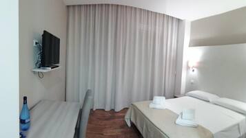 Una habitación de hotel con cama, escritorio, silla, televisor y cortina.