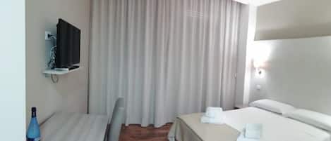 A hotel room with a bed, a desk, a chair, a television, and a curtain.