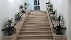 Un escalier avec des marches de couleur beige, des rampes noires et des plantes en pot de chaque côté.