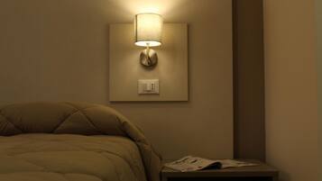 A bedroom with a bed, a nightstand, a wall-mounted lamp, and a power outlet.