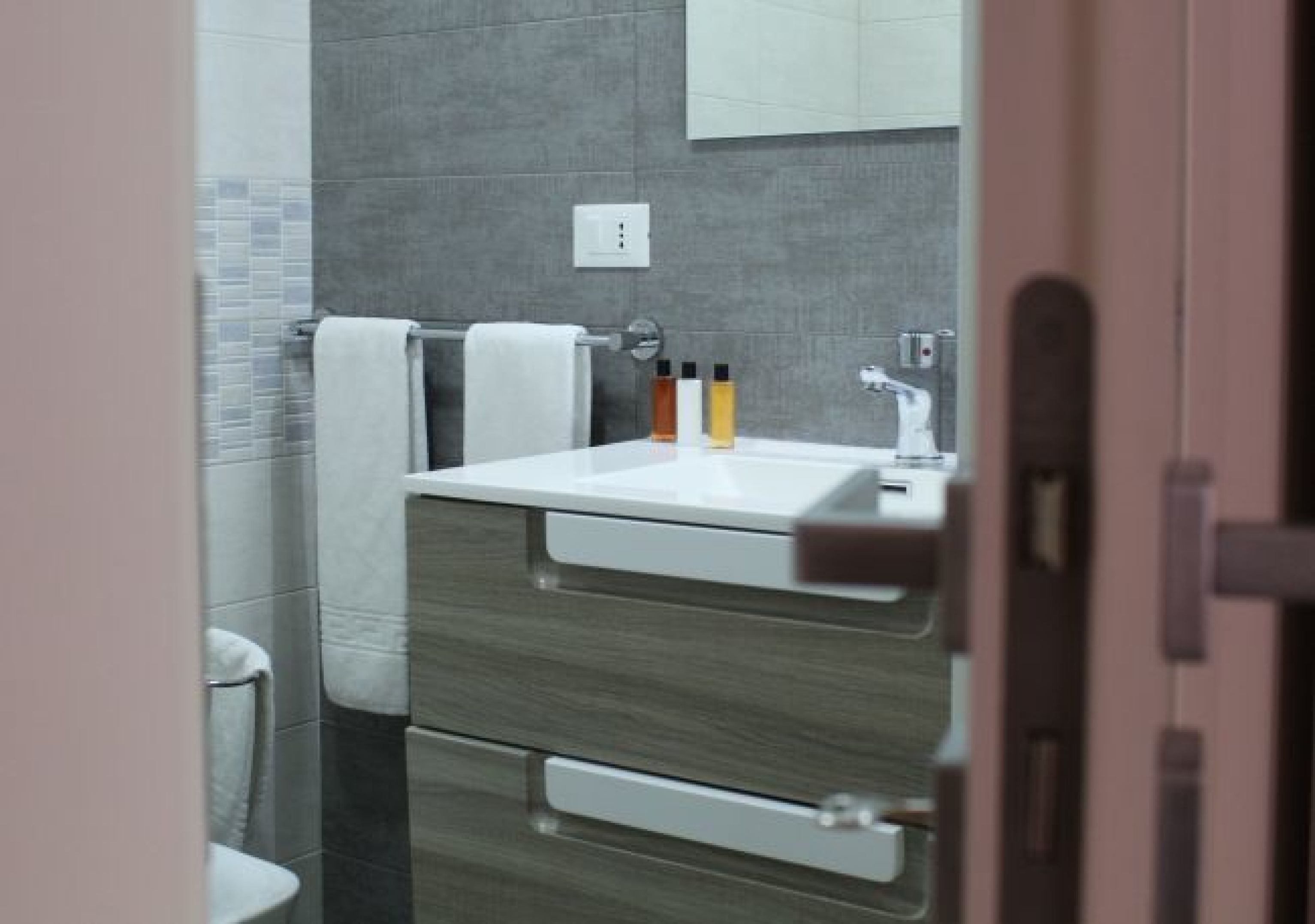 A modern bathroom with a white sink, grey tiles, and a towel rack.