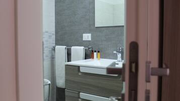 Un baño con lavamanos blanco, espejo y toallero.