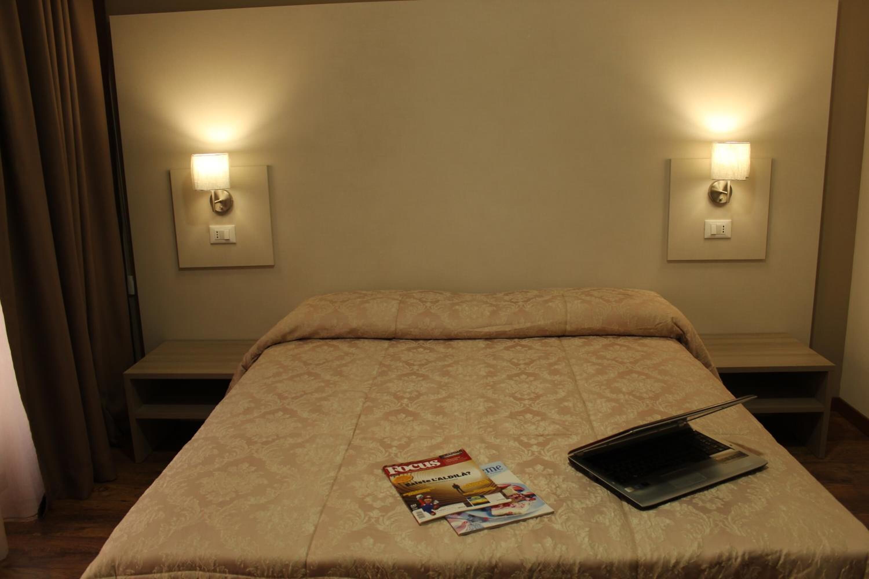 Quarto de hotel com uma cama, duas mesas de cabeceira, um laptop e uma revista sobre a cama.