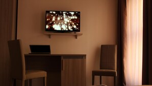 Une chambre d’hôtel avec un téléviseur fixé au mur, un bureau avec un ordinateur portable, deux chaises et un magazine sur le lit.