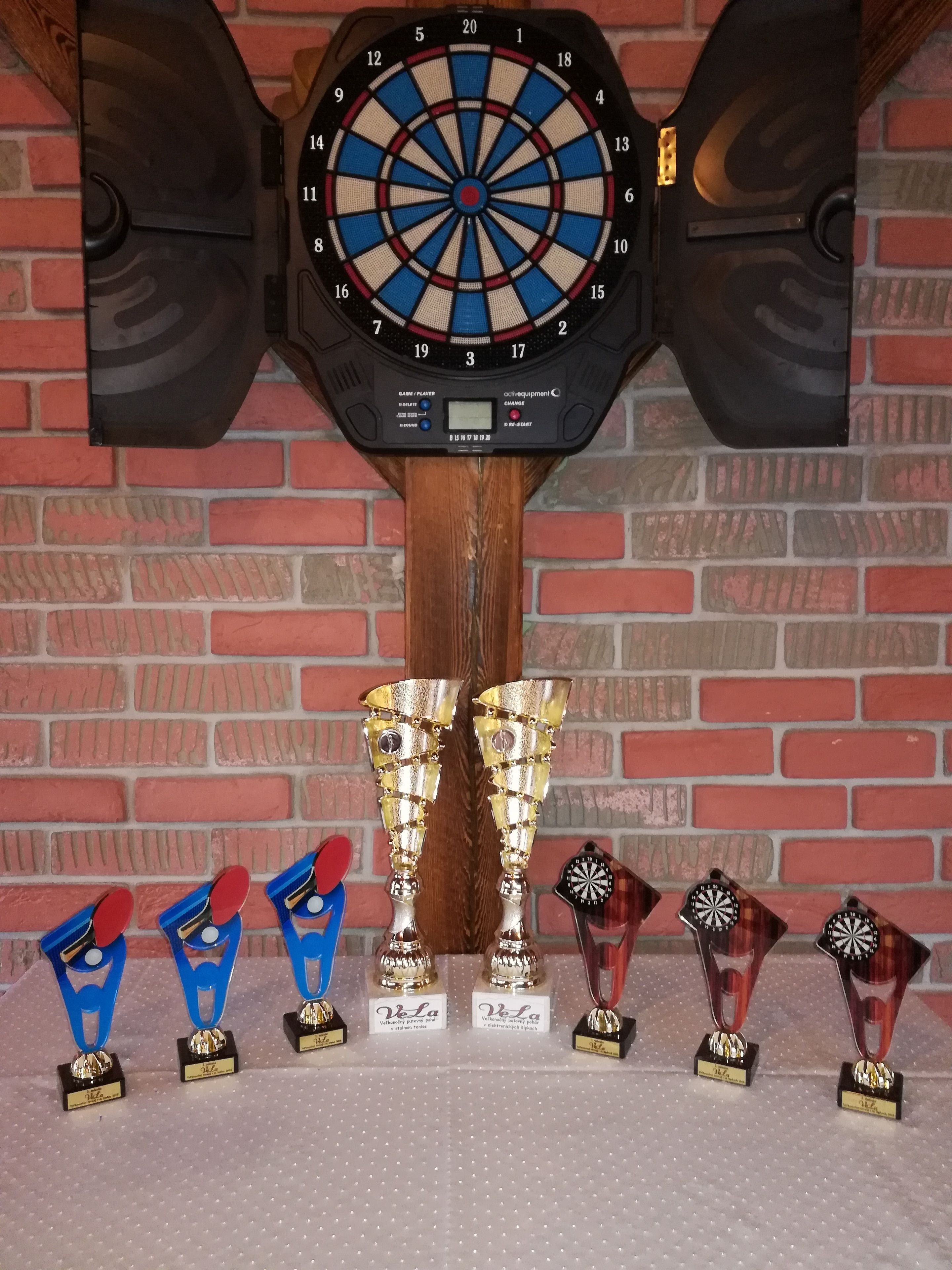Un dardo colgado en una pared de ladrillo con trofeos delante.
