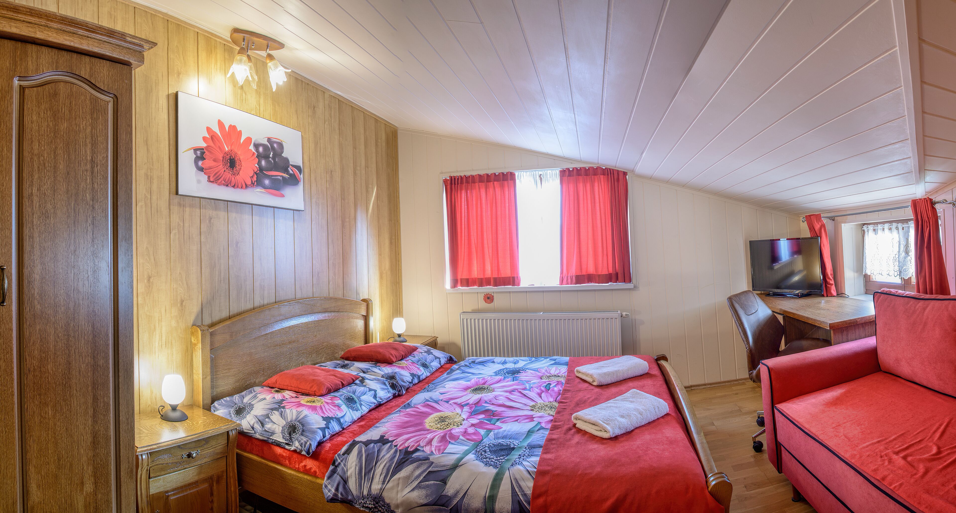 Un dormitorio con cama de cabecera de madera, un escritorio con computadora y un sofá rojo.