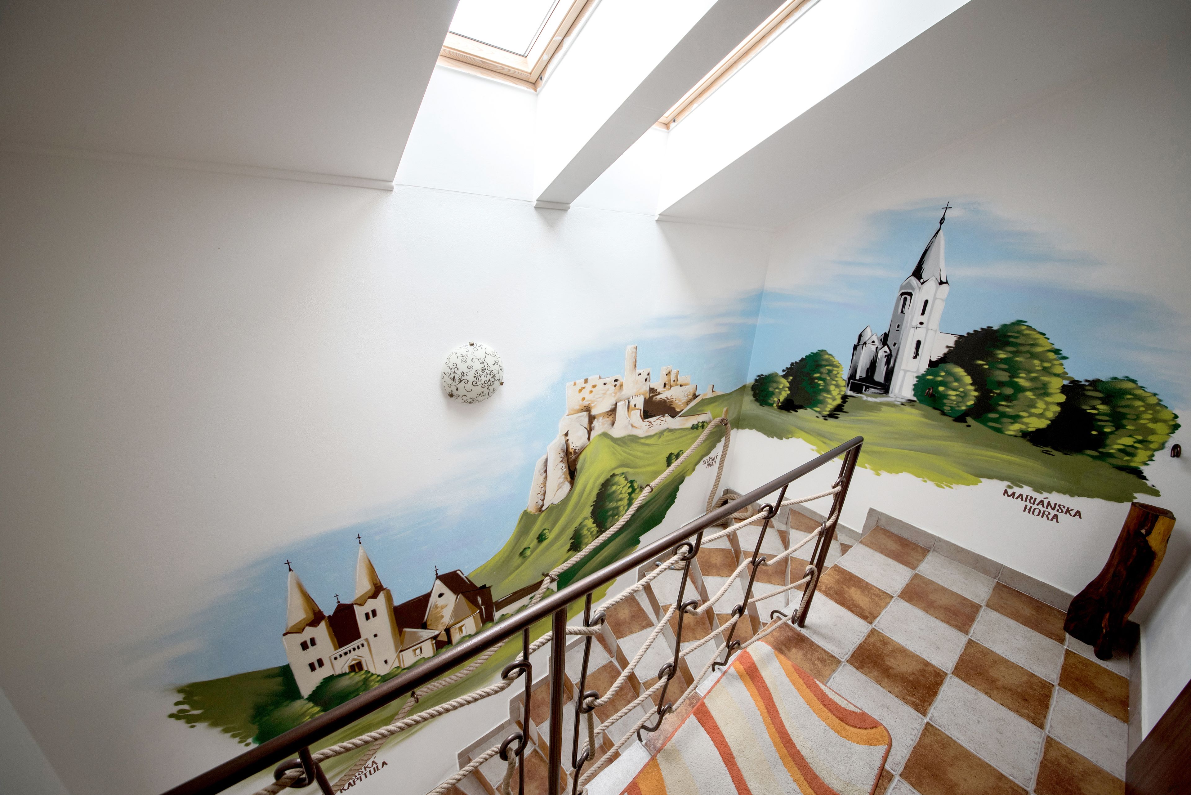 Una escalera con un mural de un castillo y una iglesia, suelo a cuadros y tragaluz.