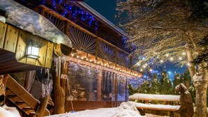 A wooden building with a snow-covered roof, string lights, and a bench in the foreground. - VeLa (Malý Slavkov)