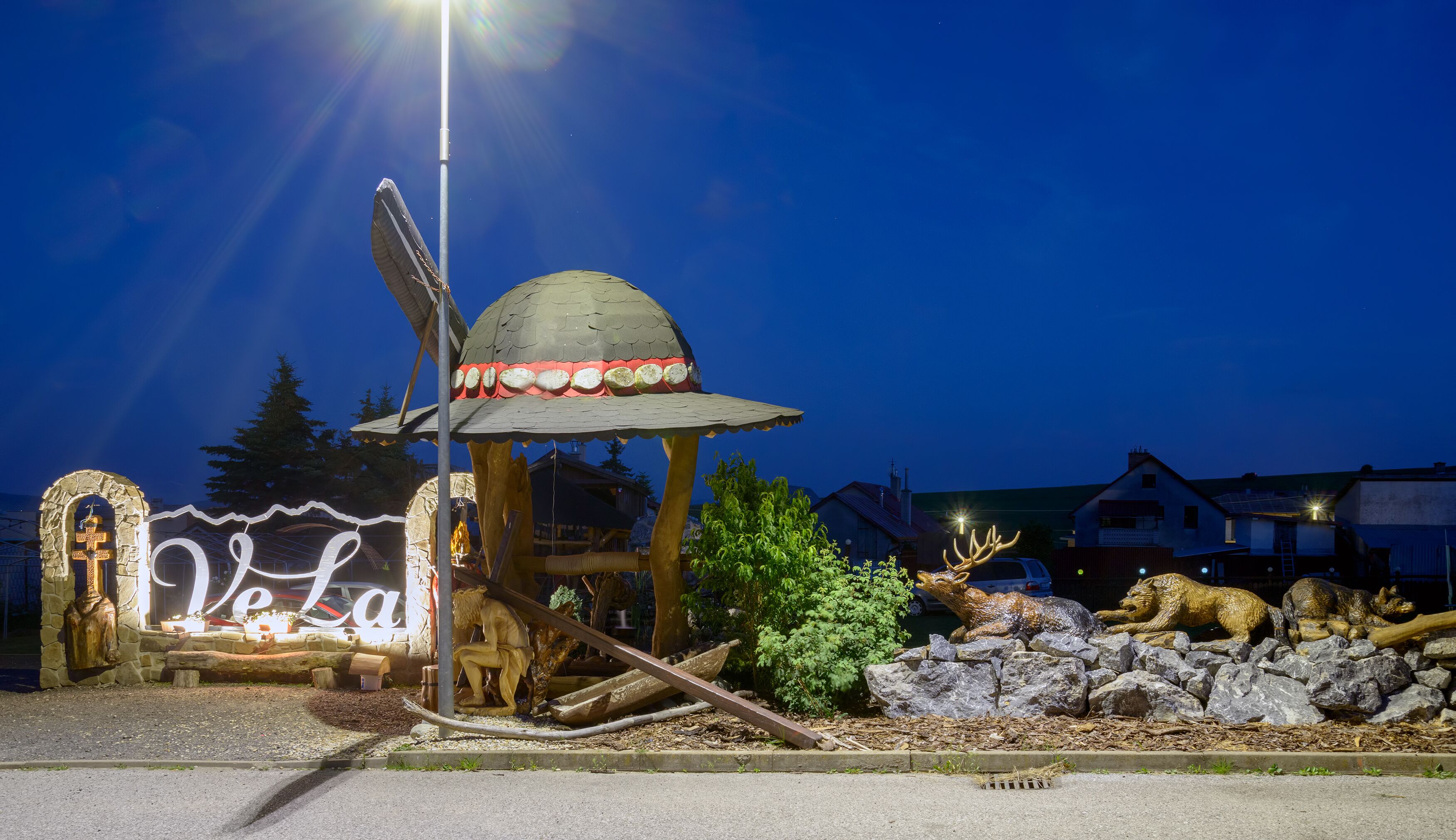 A rustic outdoor area with a wooden structure, a stone archway, and a sign that reads "Velan".