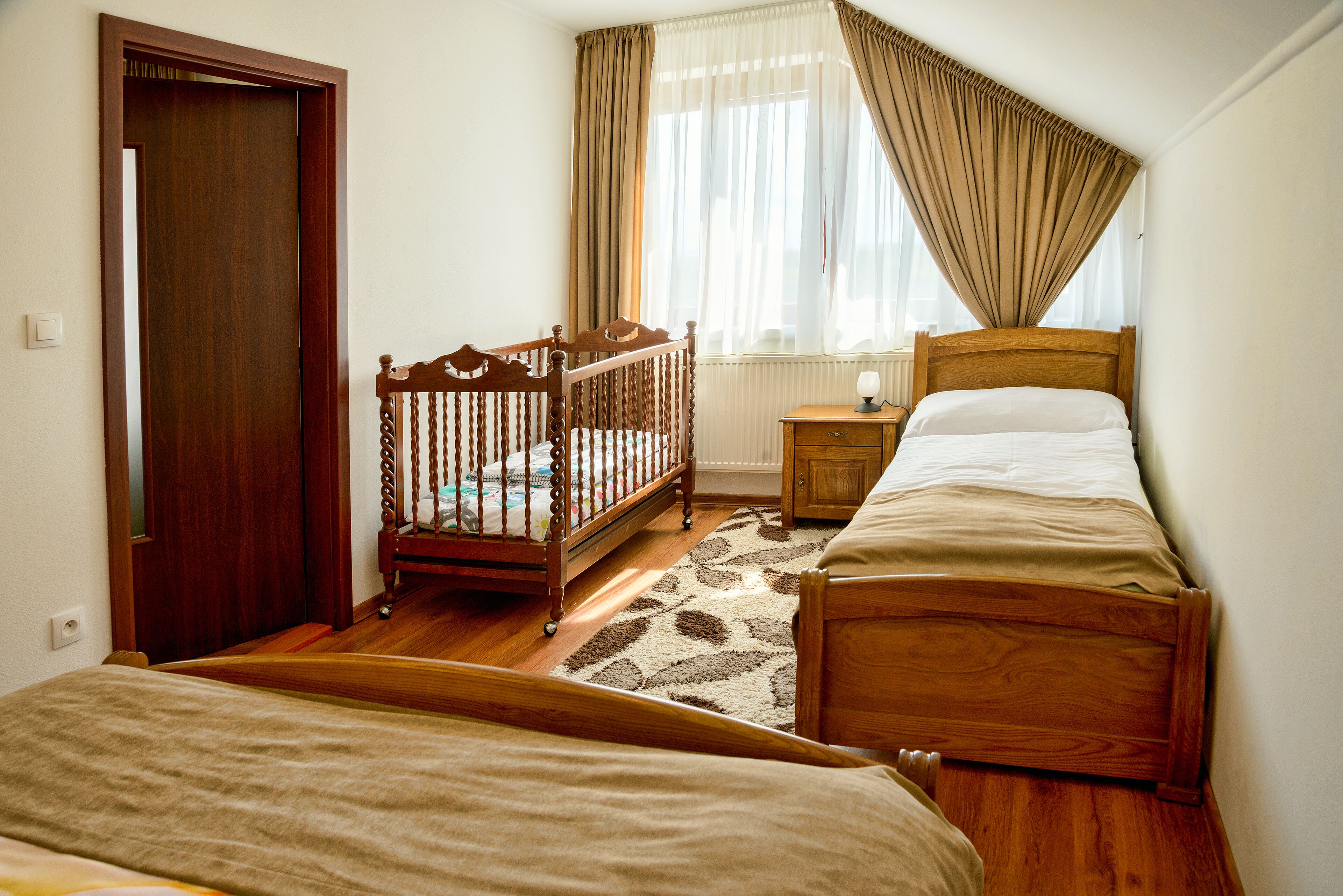A bedroom with a wooden crib, a single bed, a nightstand, and a window with curtains.