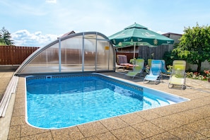 A swimming pool with a glass enclosure, surrounded by lounge chairs and a patio umbrella. - VeLa (Malý Slavkov)