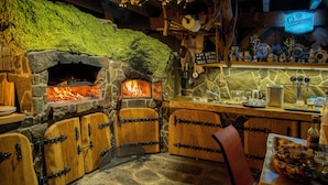 A rustic stone fireplace with a fire, wooden cabinets, and a bar area with various items. - VeLa (Malý Slavkov)
