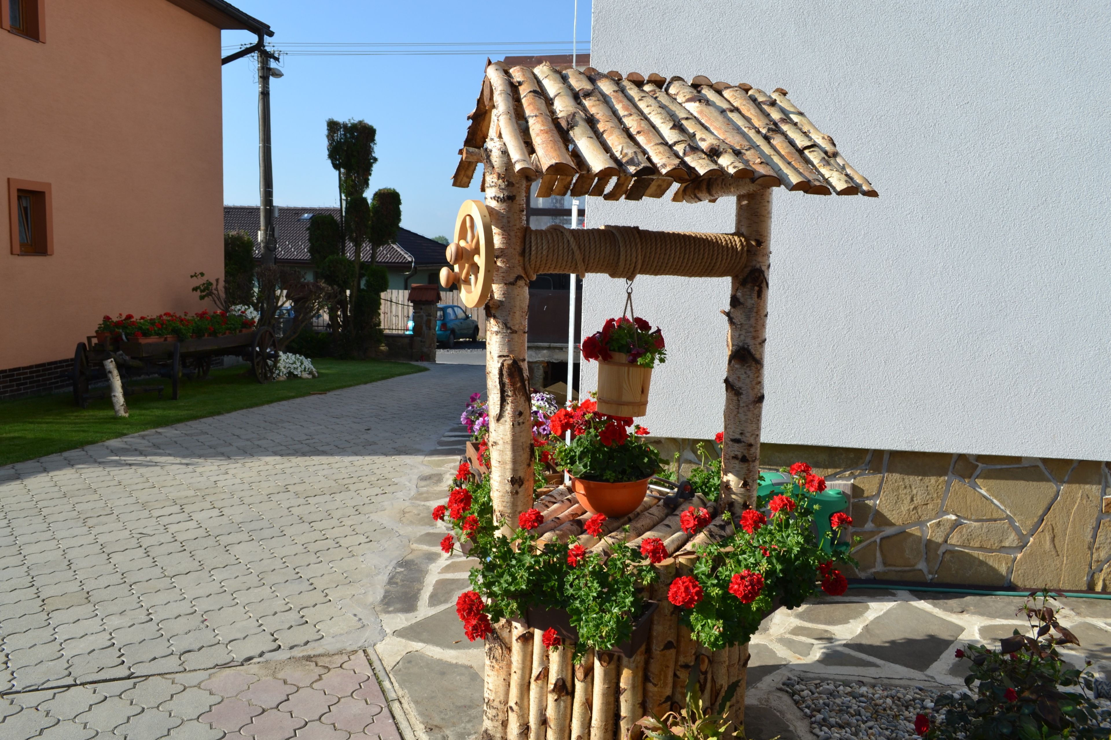 A rustic wooden gazebo with a tiled roof, surrounded by potted plants and flowers.