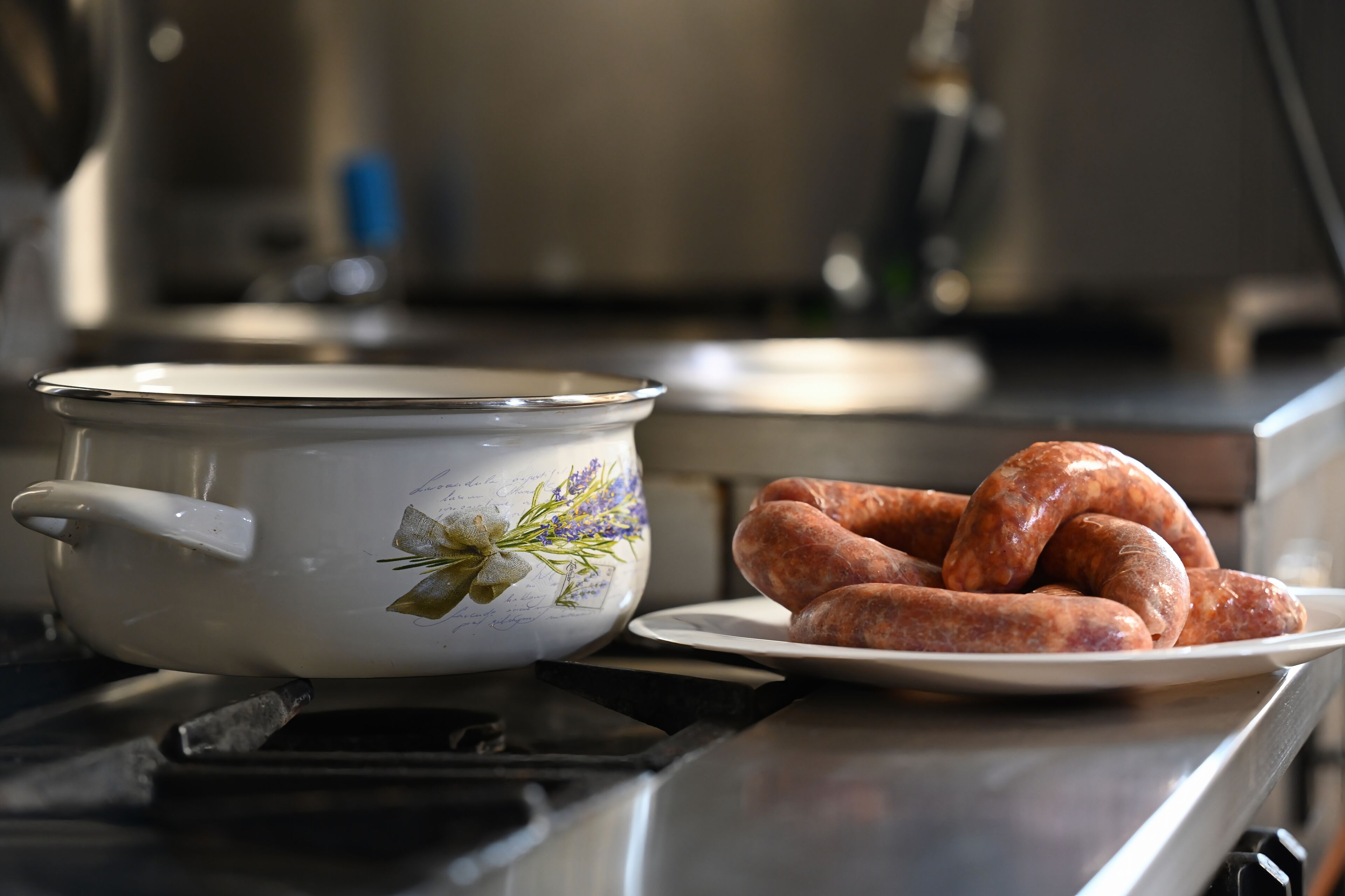 Una cocina con una olla de esmalte blanco y un plato de salchichas sobre la encimera.