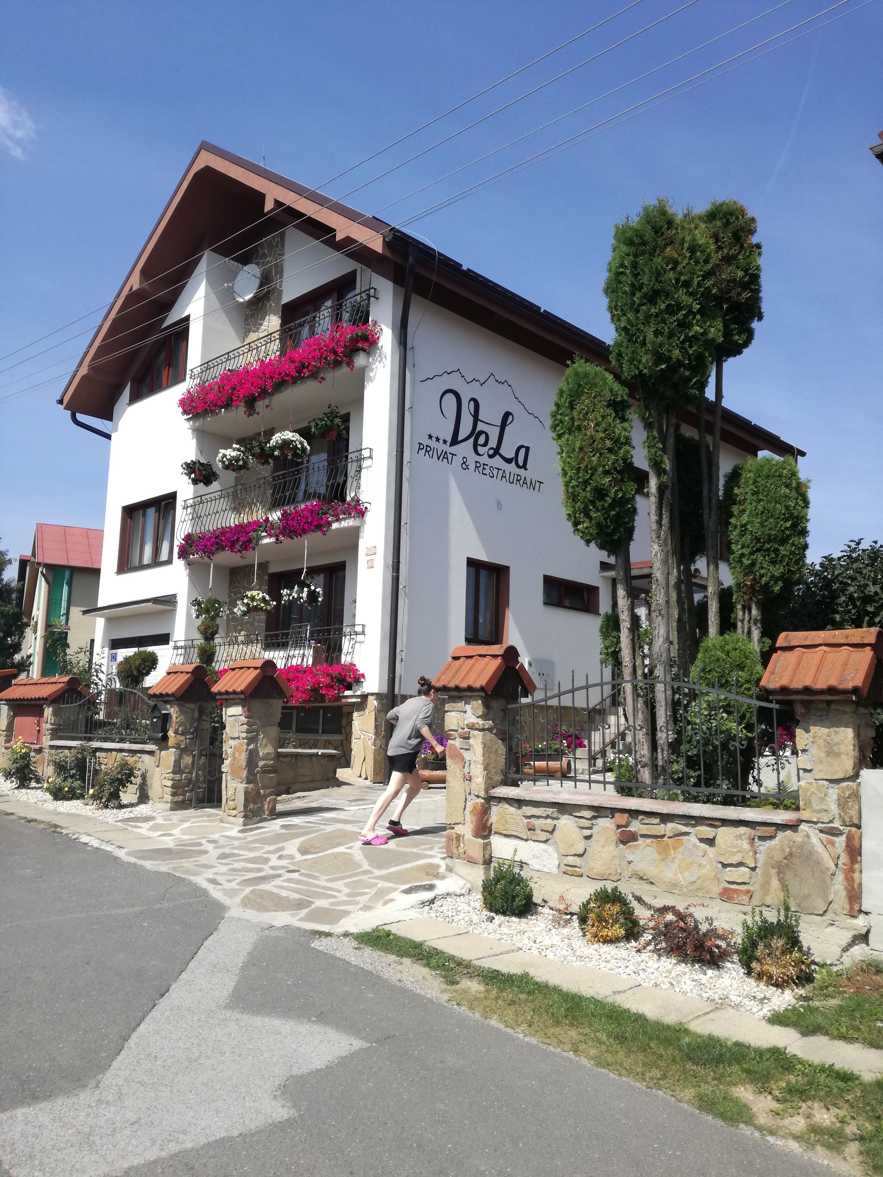 A two-story building with balconies adorned with flowers, a sign reading "Vela Privat & Restaurant," and a stone entrance.